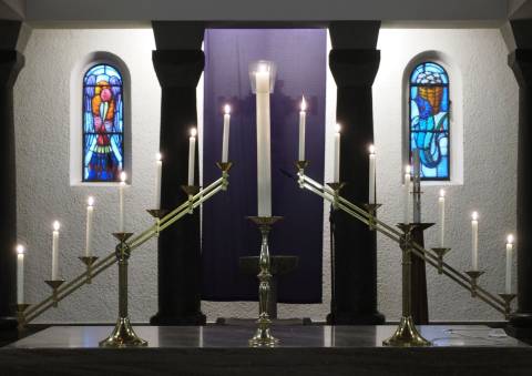 Zwei Lichtrechen mit je sieben Kerzen auf dem Altar - in der Mitte die Christus-Kerze vor dem mit einem violetten Vorhang verdeckten Kruzifix
